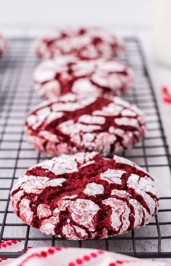 four red velvet cake mix cookies cooling on a wire rack with red and white linen. 