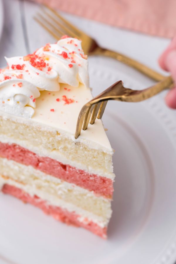 A gold fork taking a bite out of a slice of strawberry crunch cake. 