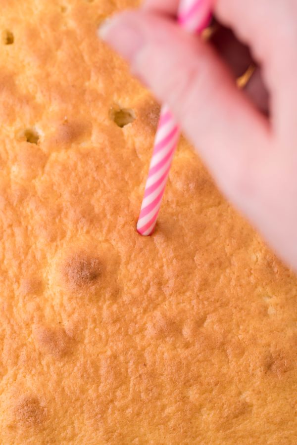 poking holes in the cake after baking using a pink and white straw. 