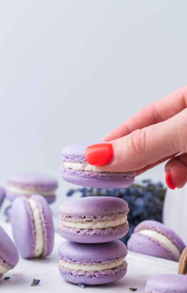 A manicured hand stacking a lavender macaron on top of two others