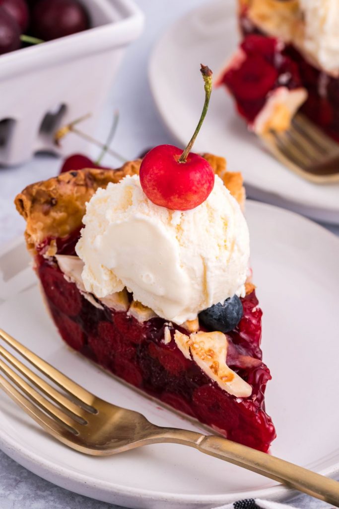 A slice of cherry pie topped with vanilla ice cream and a fresh cherry. 