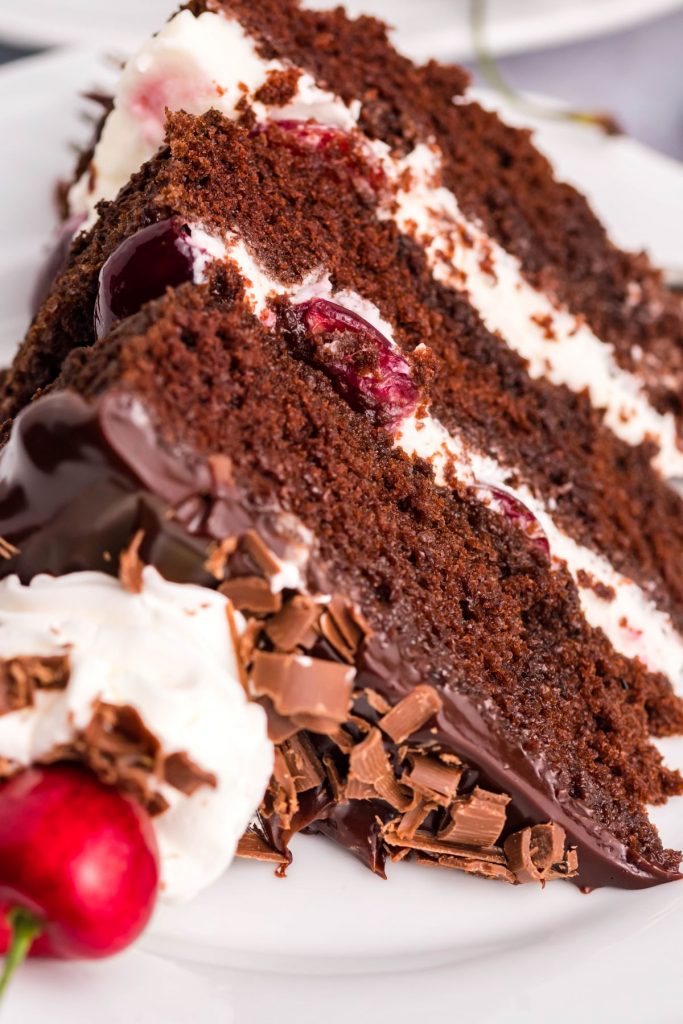 A close up of a slice of German Black Forest Cake on a white plate with a silver fork. 