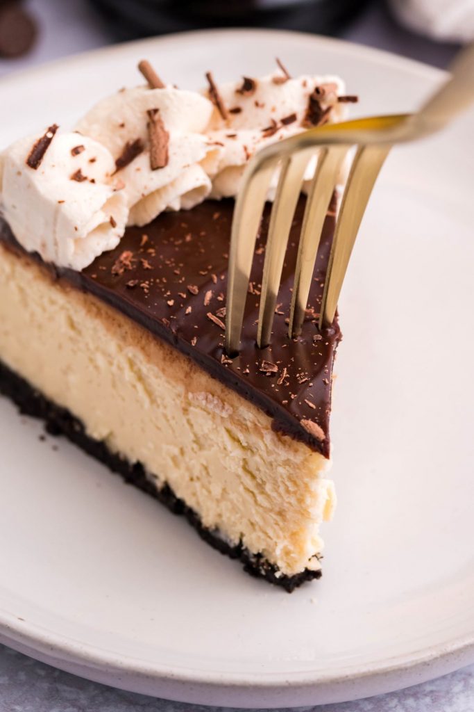 Slice of Kahlua Cheesecake on a white plate with a bite being removed with a gold fork.