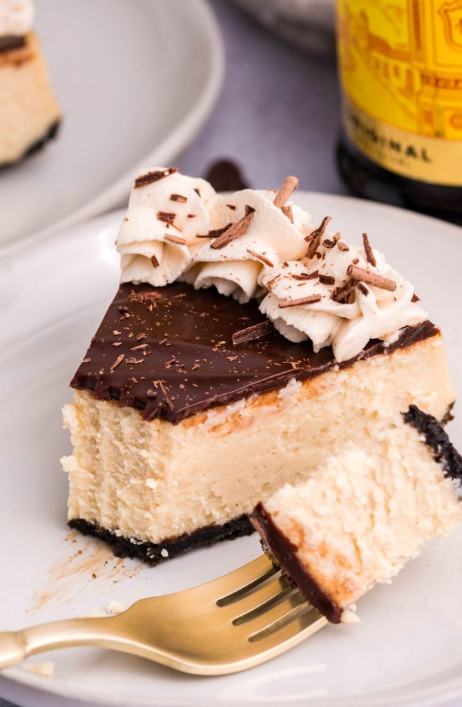 Slice of Kahlua Cheesecake on a white plate with a bite being removed with a gold fork.