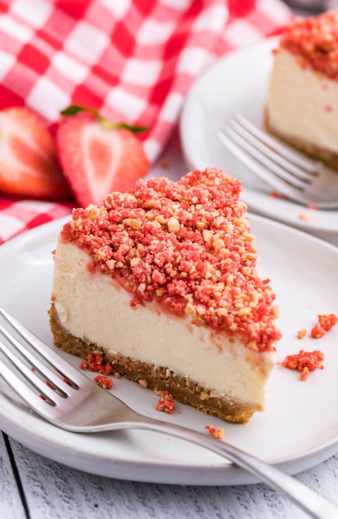A piece of strawberry crunch cheesecake on a white plate with a silver fork. 
