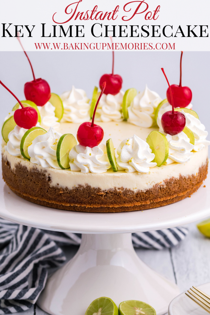 An Instant Pot Key Lime Cheesecake on a white cake stand with a black and white linen and limes in the background. Topped with sliced limes, whipped cream, and cherries.