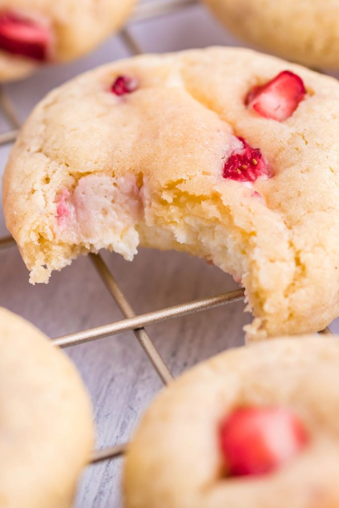 A Strawberry cheesecake cookie with a bite removed on a gold wire rack.