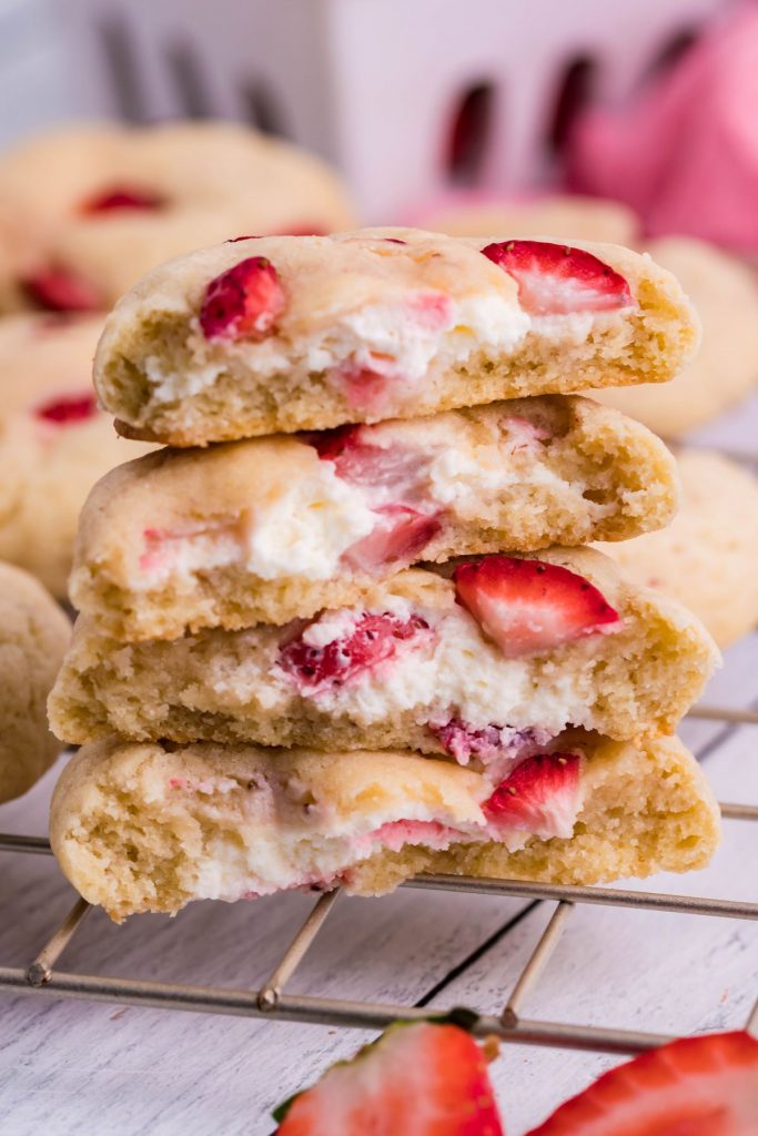 4 strawberry cheesecake cookies cut in half and stacked on a gold wire rack. Fresh strawberries peaking in from the side.  
