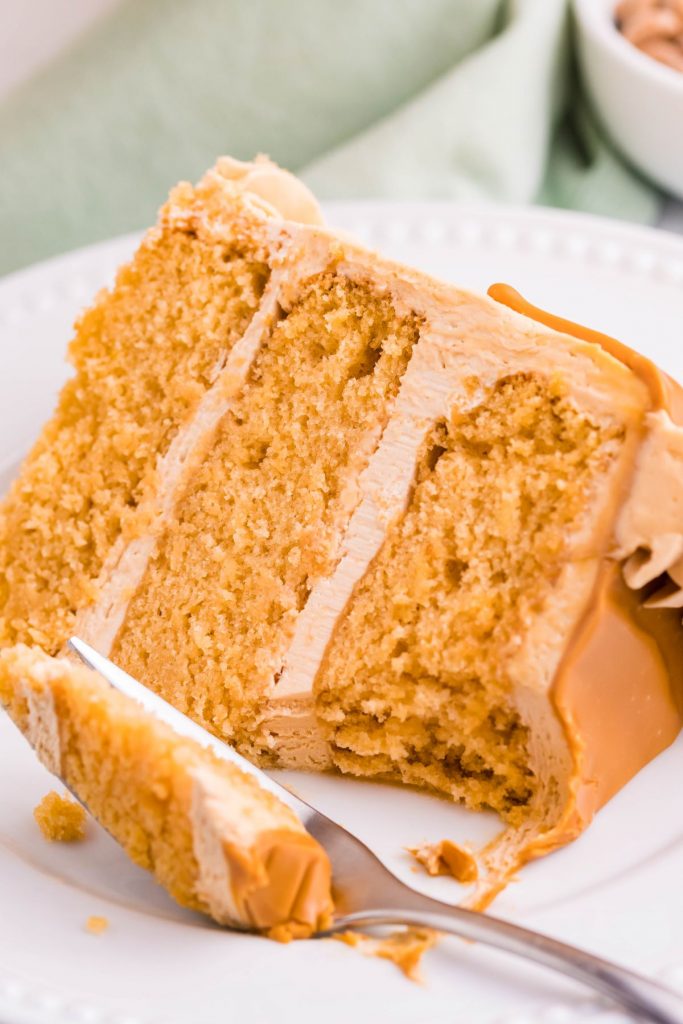 A piece of butterscotch cake on a white plate with a silver fork with a bite removed. 