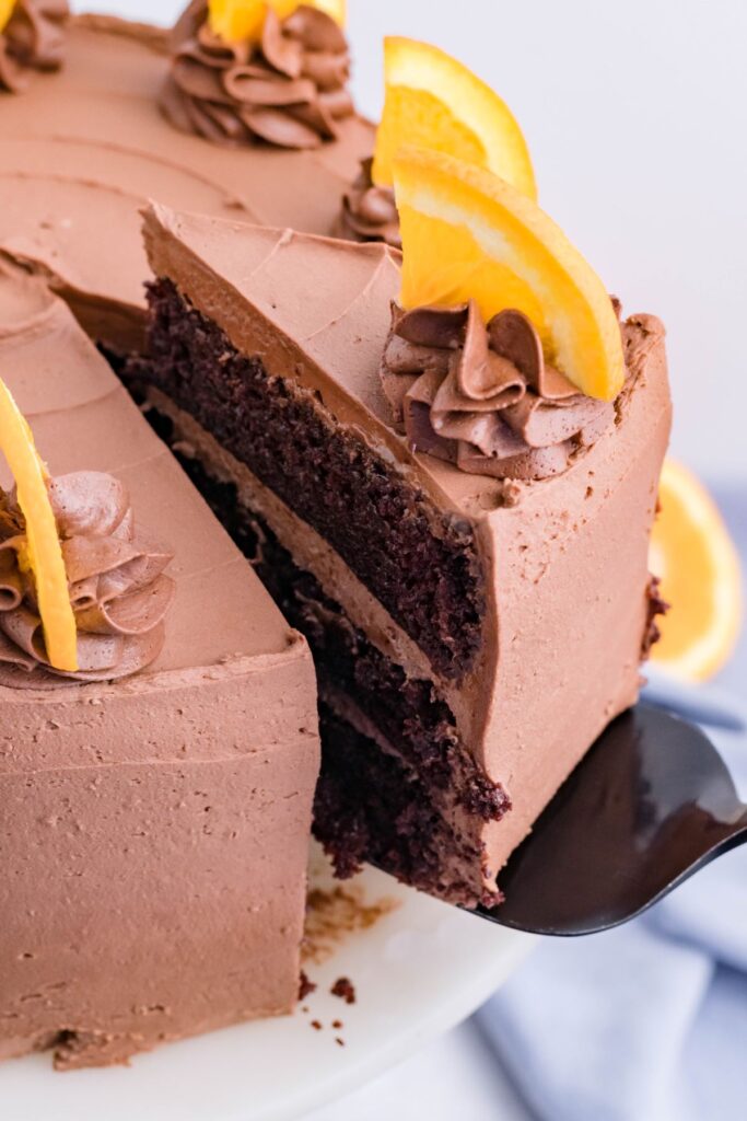 A piece of chocolate orange cake being removed using a black spatula with sliced oranges in the background. 