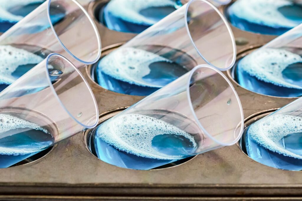 Tall shot glasses on their side in a muffin tin with blue jello layer. 