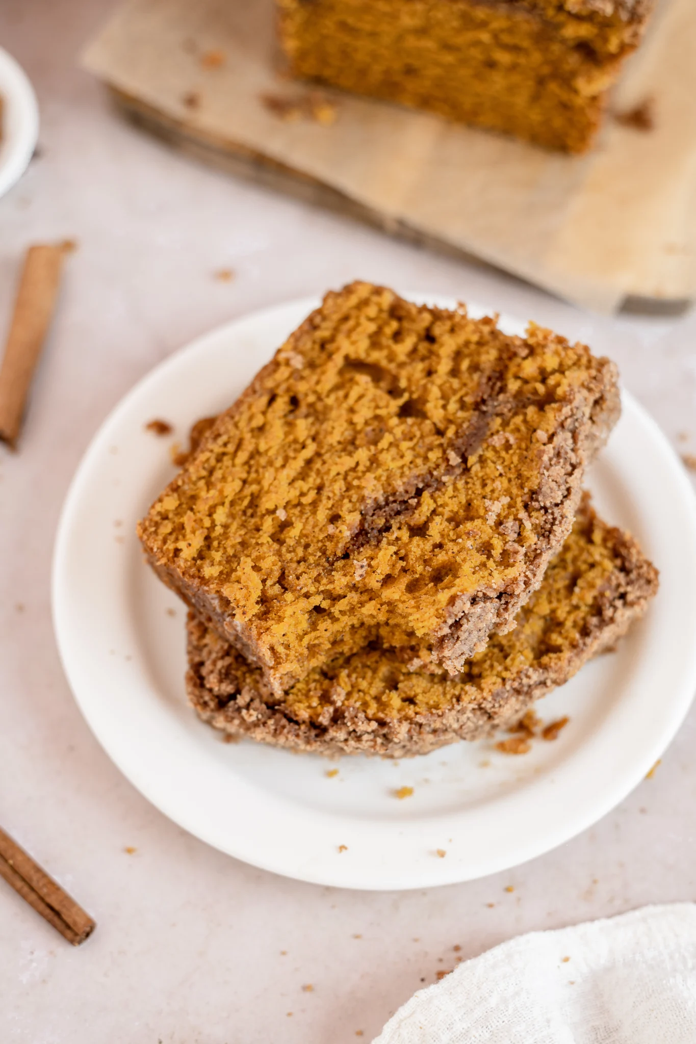 Two slices of pumpkin bread with streusel on a white plate on a light pink background. 