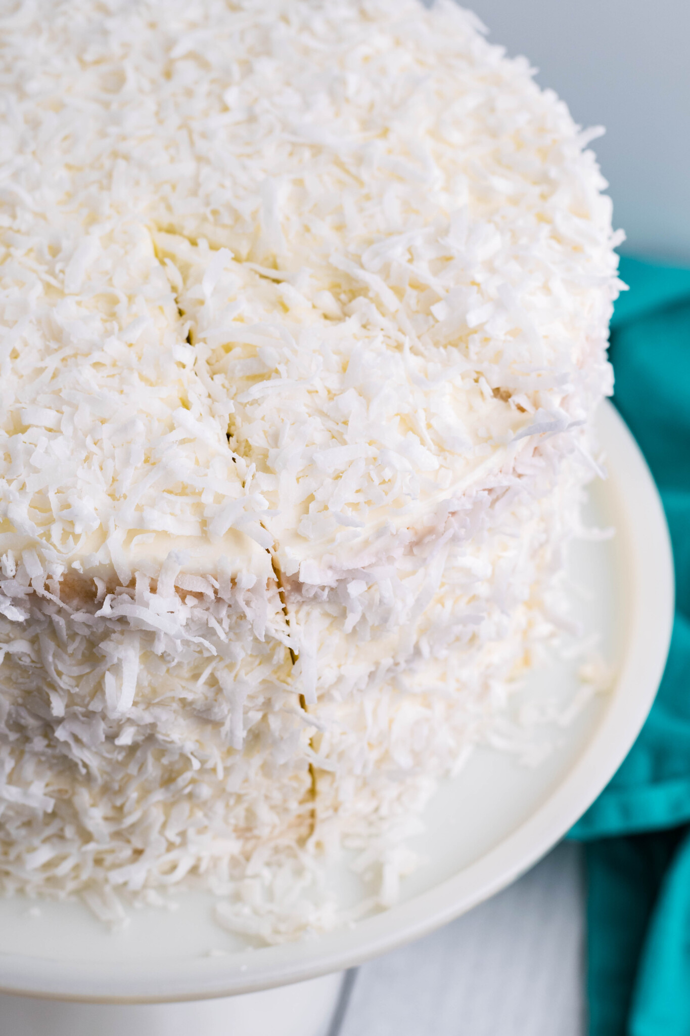 Close up view of Coconut Cake on a white cake stand with a slice cut.