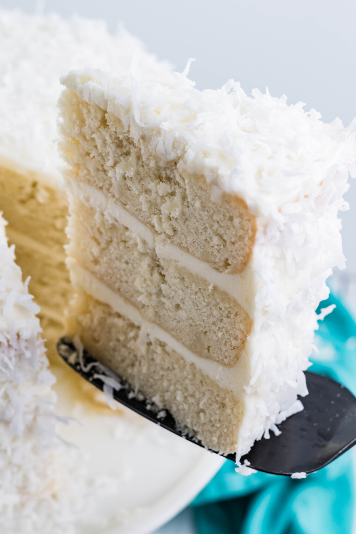 Close up view of a black cake server removing a slice of Coconut Cake.