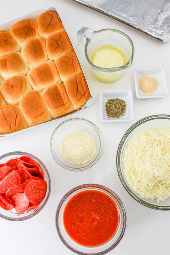 ingredients for pepperoni sliders on a table with a foiled wrapped tray behind it 