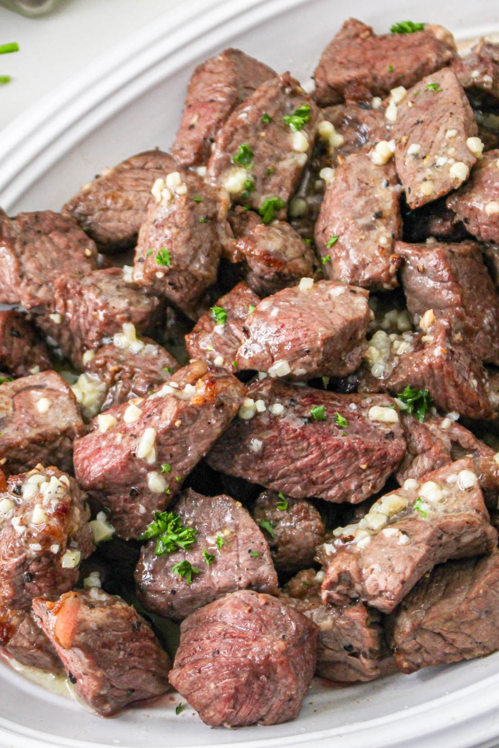 steak diced into pieces cooked and in a white platter with a drizzle of butter and garlic on top 