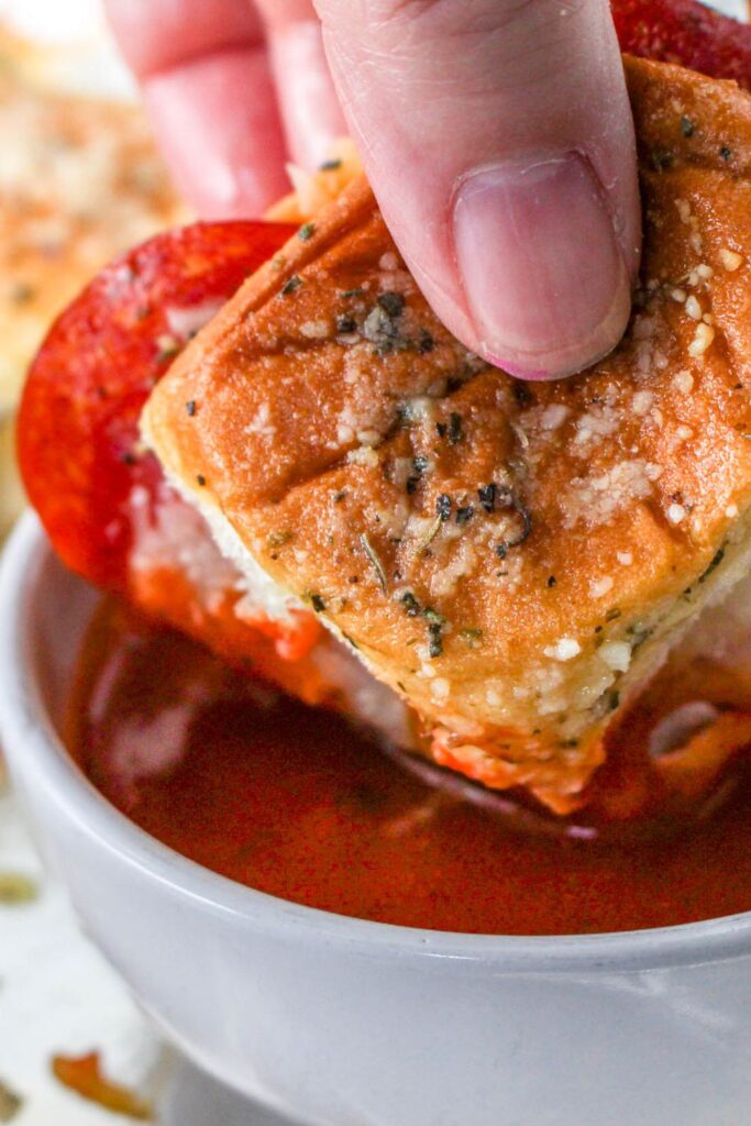 dipping a pizza slider in hand into a bowl of pizza sauce 