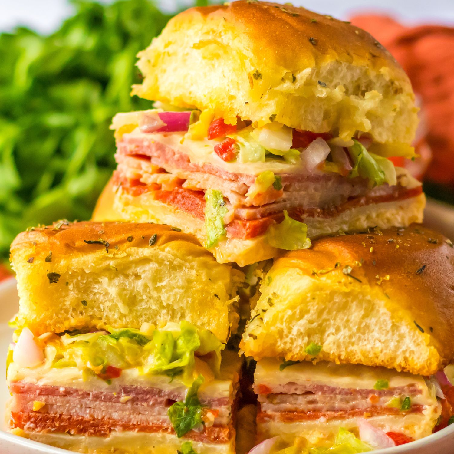 Italian subs stacked on a plate with lettuce and other produce in the background